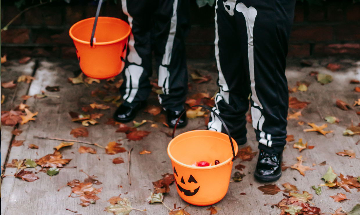 Kids in skeleton Halloween costumes with pumpkin buckets of candy