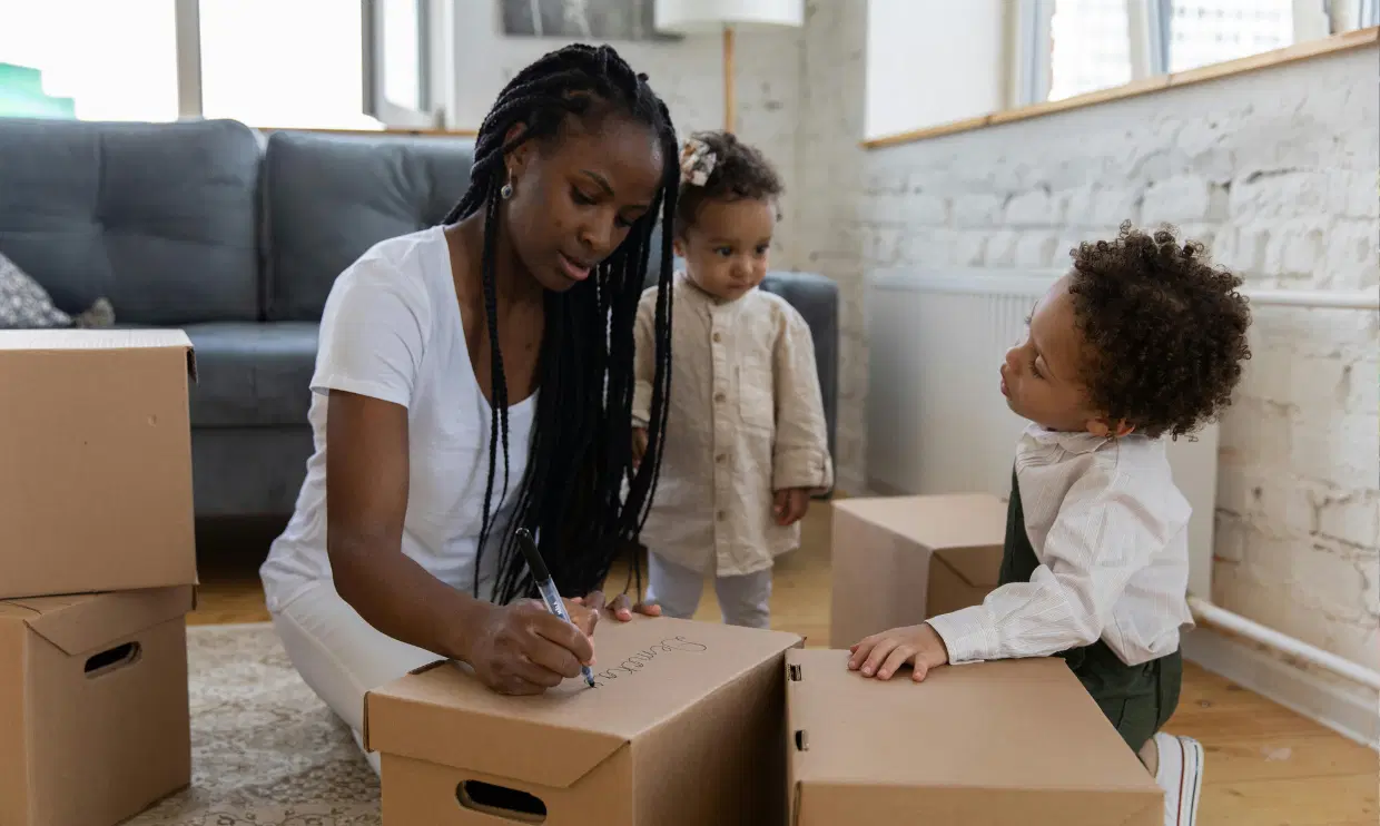 Parent writing on cardboard boxes with two kids